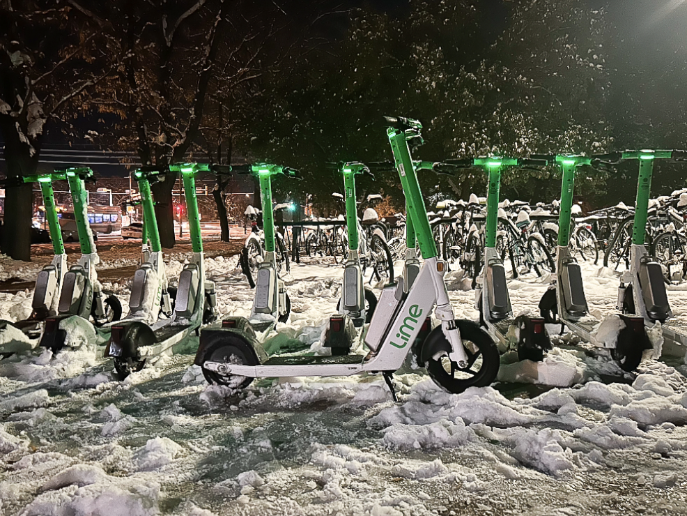 Three Lime scooters parked in the snow off a main road in Boulder, Colorado.